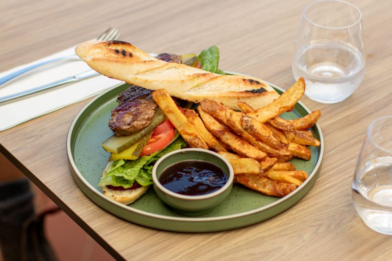 Steak sandwich with thick cut fries and barbeque presented beautifully on a green plate, set on a table with cutlery and a glass of water
