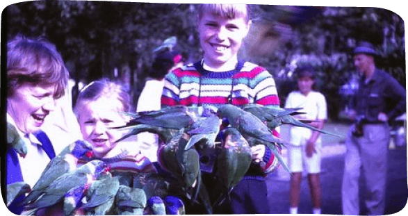 A boy and girl joyfully hold green birds, showcasing their delight in nature and companionship
