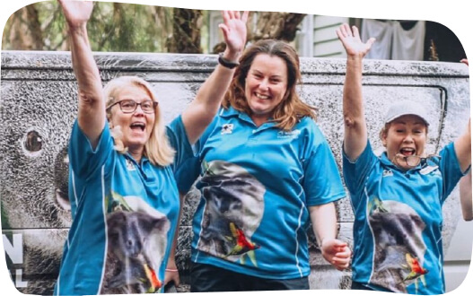Three women in blue shirts joyfully waving at the camera, showcasing a friendly and welcoming atmosphere.