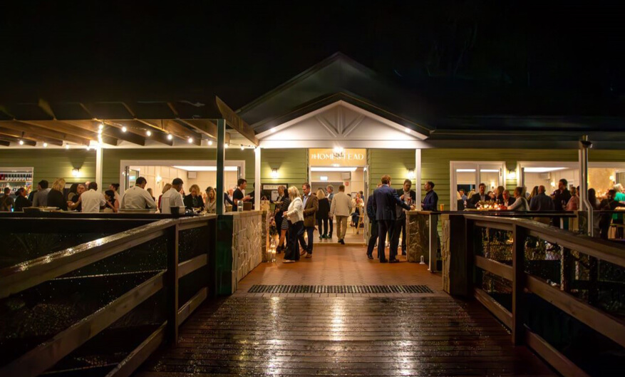 Outdoor event at the Home Stead venue at night, with people mingling on a covered patio.