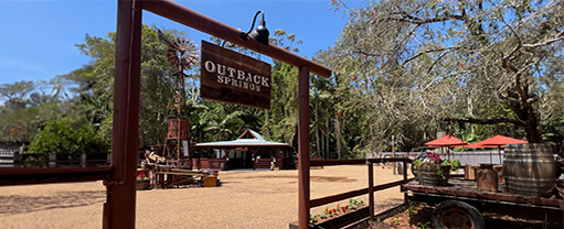 Outdoor view of Outback Springs, a rustic-themed venue with a wooden sign, a small pavilion, and a vintage-style wagon.