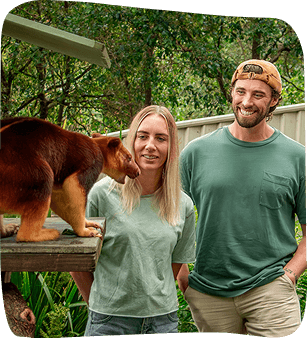 Couple interacting with a reddish-brown animal in a shaded outdoor enclosure.