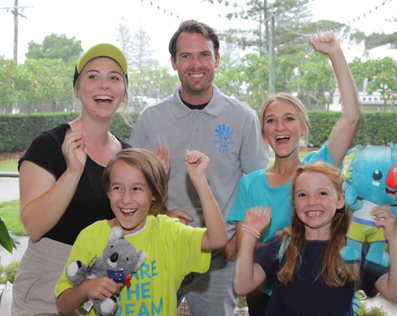 Excited family and friends, including children, celebrate a sporting event or achievement, with raised arms and smiles.
