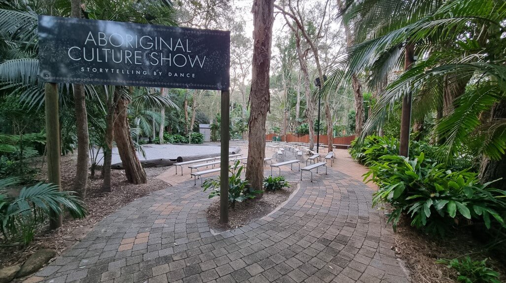 An outdoor performance area surrounded by lush greenery, featuring a sign that reads 'ABORIGINAL CULTURE SHOW STORYTELLING BY DANCE.'