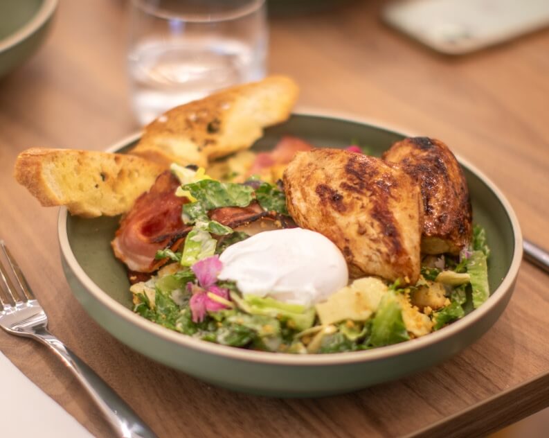 Grilled chicken caesar salad bowl with croutons, bacon, and poached egg.