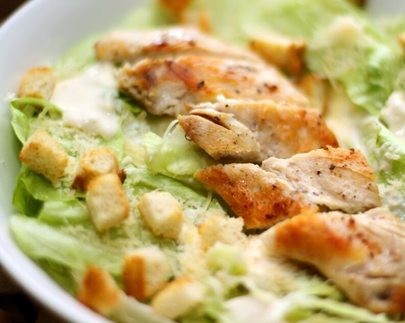 A fresh Caesar salad topped with golden-brown grilled chicken pieces, crunchy croutons, and drizzled with creamy Caesar dressing.