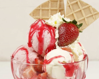 A bowl filled with creamy ice cream topped with fresh strawberries and a generous swirl of whipped cream