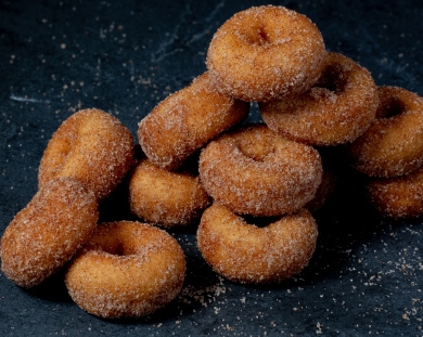 A stack of small, round donuts coated in a cinnamon-sugar mixture, arranged in a pyramid-like fashion on a dark surface.