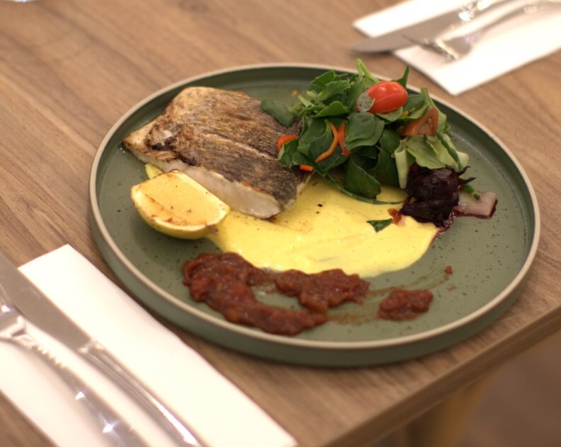 Grilled fish dish with lemon, sauce, and mixed greens on a green plate.