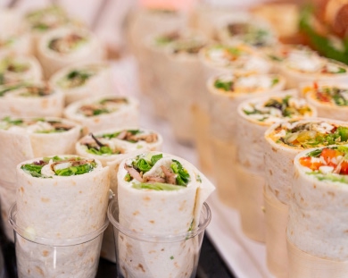 Multiple clear plastic cups filled with colorful wraps. Each wrap contains various fillings, like vegetables, greens, and possibly meats.