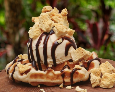 A delicious dessert is presented on a wooden surface. It features a freshly made waffle topped with a scoop of vanilla ice cream.