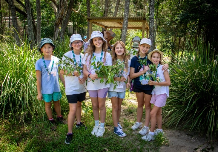 Group of girls in nature, holding branches, smiling and posing outdoors.