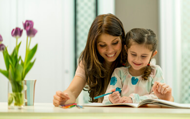 Mother and daughter, smiling, color a book together at a table.