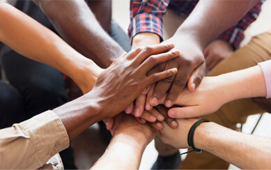 Diverse group of people with hands clasped together in a circle.