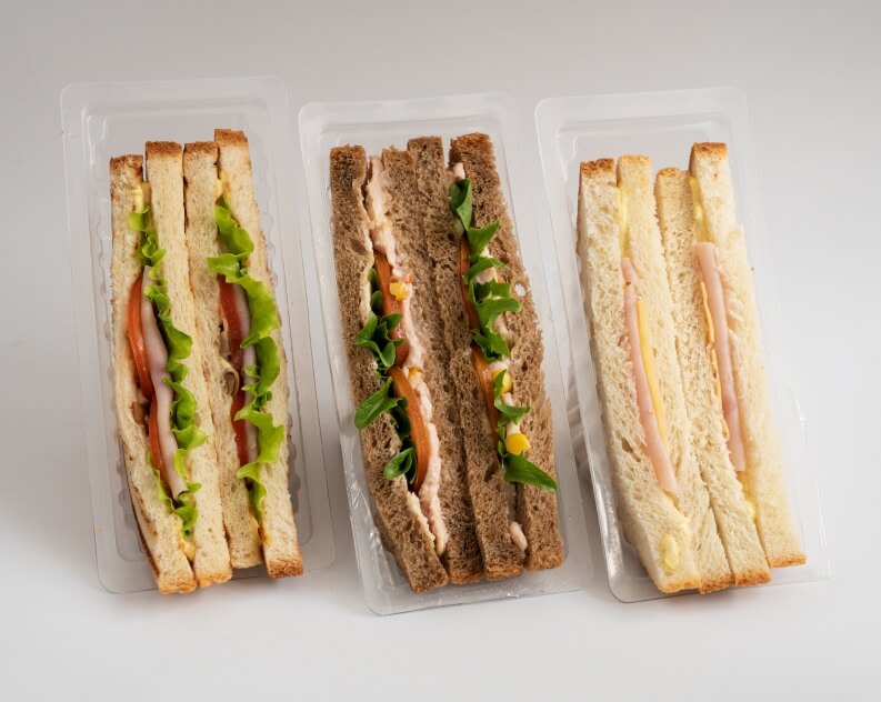 Three different packaged sandwiches neatly placed side by side in clear plastic containers.