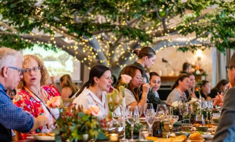 A group of people gathered around a long dining table adorned with decorative elements like flowers, candles, and glassware.