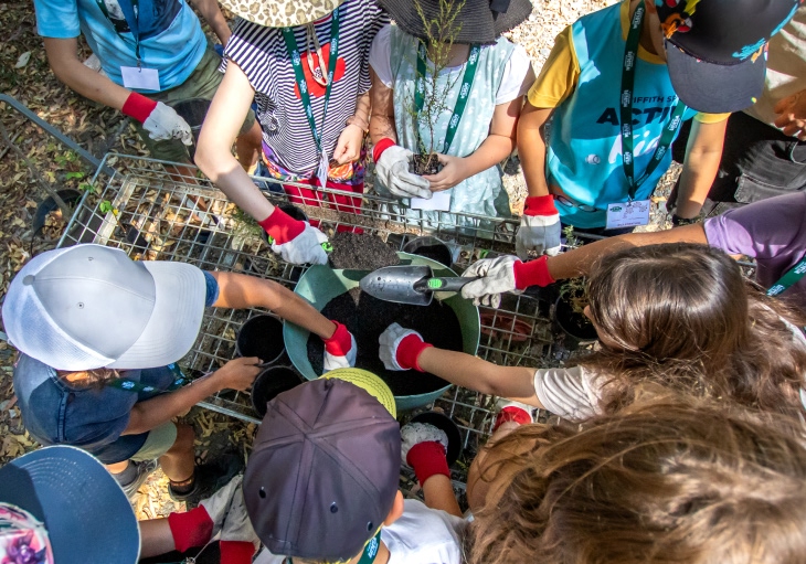Group of children wearing gloves, planting seedlings in containers on a metal cart.
