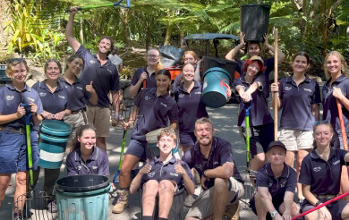 Group of zookeepers in uniform, holding cleaning supplies, participating in a park cleanup.