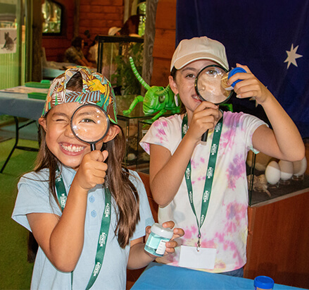 Two children, smiling and holding magnifying glasses, explore insects at a natural history museum.