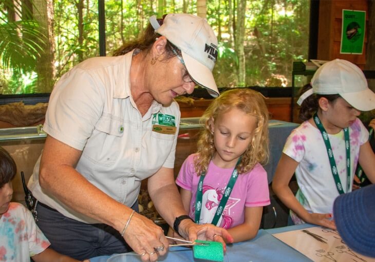 A woman volunteer demonstrates bandage application to two children at a wildlife conservation center.