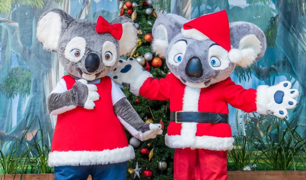 two people dressed in christmas themed koala costumes standing on a stage posing with arms out