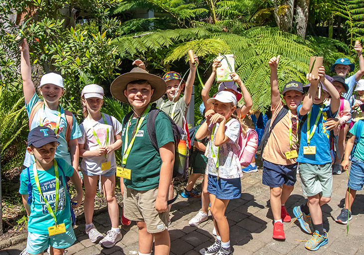 Group of school kids making funny poses and smiling in front of large lush ferns