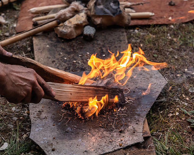 Closeup of a person using wooden sticks and fibres to make a fire on a sheet laying on grass