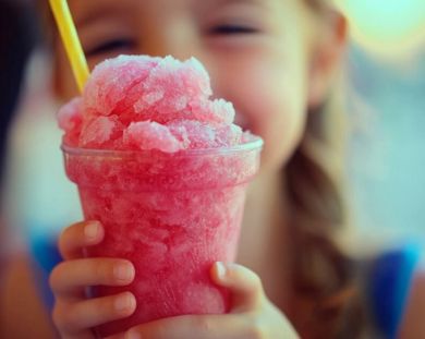 Pink slushie in a clear cup being held by a young girl