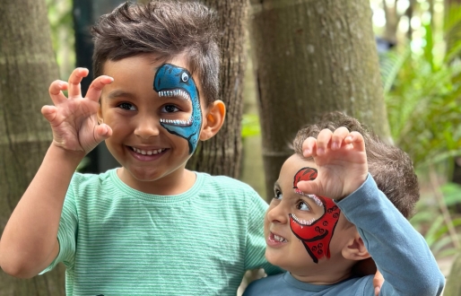 Two young boys with dinosaurs painted on their face, smiling and making roaring gestures