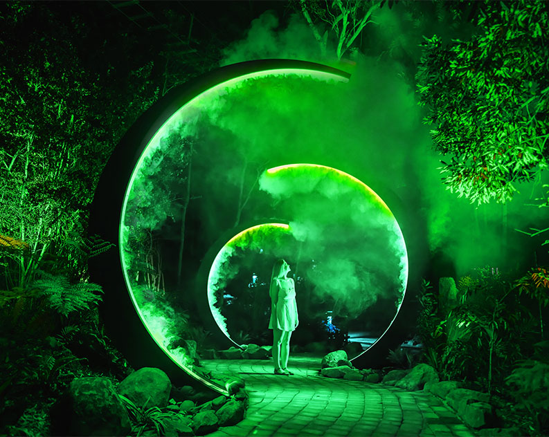 Girl standing on a paved stone path at night underneath three half moon circles emanating green lights and fog