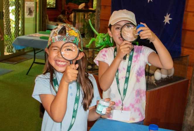 Two girls smiling and holding magnifying glasses, explore insects at a natural history museum.