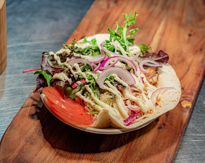 An open chicken salad wrap topped with sauce served on a wooden board
