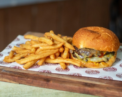 A beef burger with a side of thick cut hot chips served on a wooden plate covered with a paper bottom