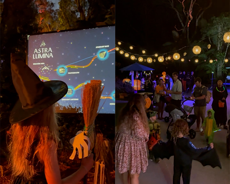 Child in a witch hat holding a broom at the Astra Lumina trail map, beside families and kids in bat and dinosaur costumes under festoon lights